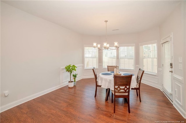 dining room featuring a healthy amount of sunlight, dark wood-style floors, a decorative wall, and a notable chandelier