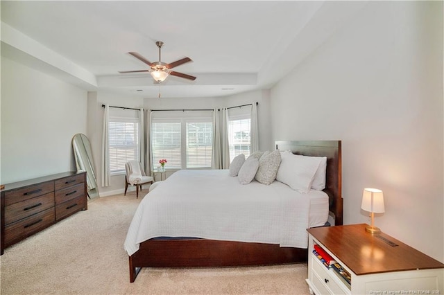 bedroom with light carpet, a tray ceiling, a ceiling fan, and baseboards