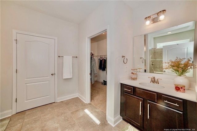 bathroom with a spacious closet, baseboards, walk in shower, and vanity