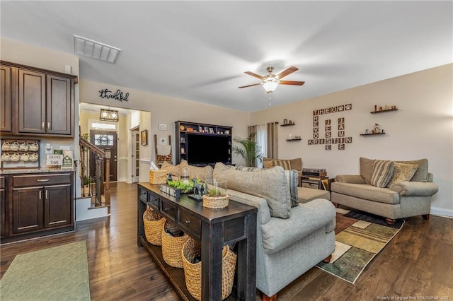 living room with visible vents, baseboards, ceiling fan, stairway, and dark wood-type flooring