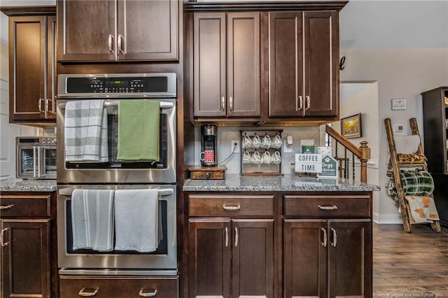 kitchen with double oven, backsplash, dark brown cabinets, and light stone countertops