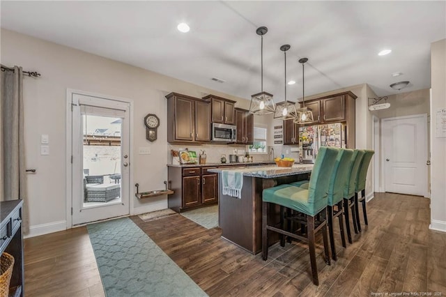 kitchen with a breakfast bar, dark wood-style flooring, a center island, appliances with stainless steel finishes, and dark brown cabinets