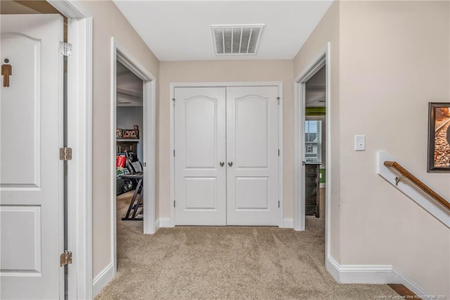 hallway featuring baseboards, visible vents, light carpet, and an upstairs landing