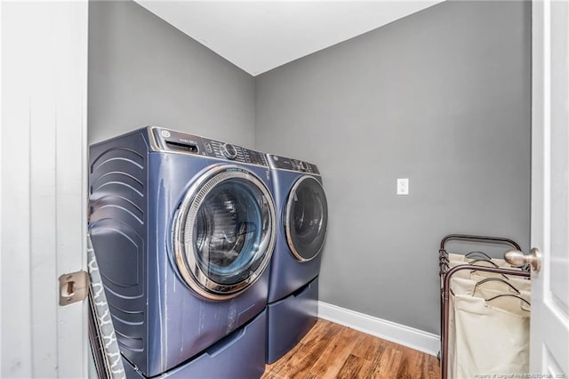 clothes washing area with laundry area, baseboards, washer and dryer, and wood finished floors