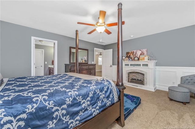 carpeted bedroom featuring a fireplace, a decorative wall, a ceiling fan, wainscoting, and connected bathroom