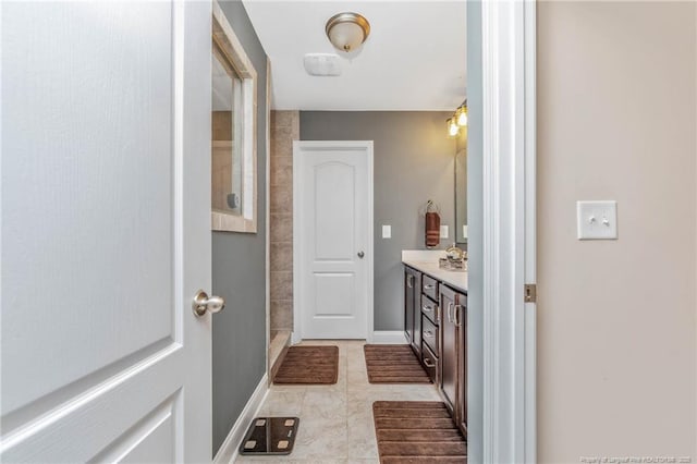 full bathroom featuring tiled shower, vanity, and baseboards