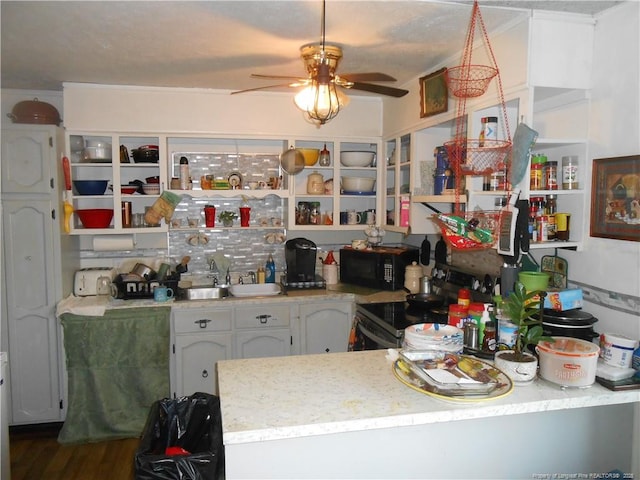 kitchen featuring black microwave, a sink, stainless steel range with electric cooktop, light countertops, and open shelves