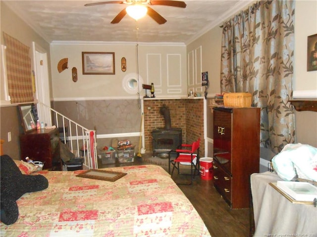 bedroom featuring a wood stove, a ceiling fan, crown molding, and wood finished floors