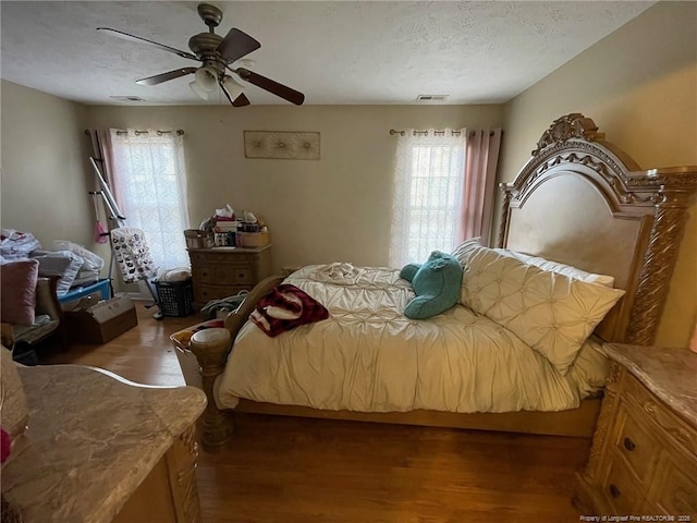 bedroom featuring dark wood-type flooring, visible vents, a textured ceiling, and a ceiling fan