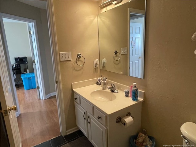 bathroom with a textured wall, toilet, wood finished floors, vanity, and baseboards