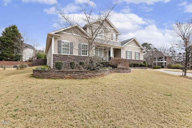 view of front of house featuring stone siding, covered porch, a front yard, and fence