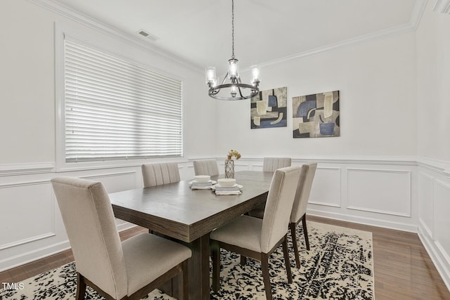 dining area with visible vents, ornamental molding, wood finished floors, a decorative wall, and a chandelier