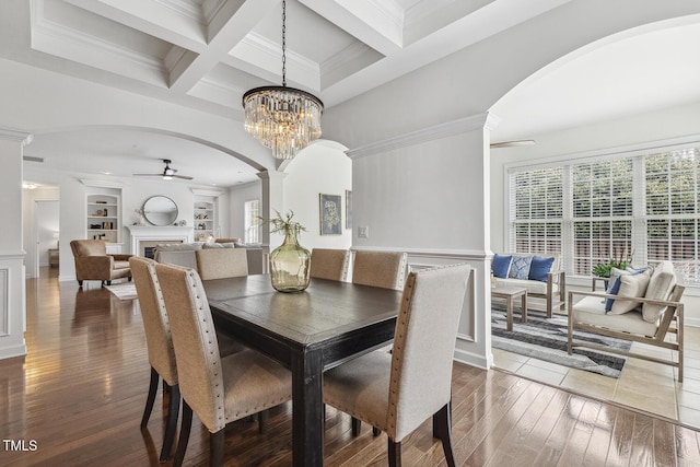 dining room featuring a ceiling fan, built in features, hardwood / wood-style floors, arched walkways, and a fireplace