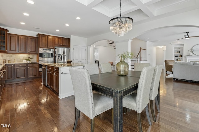 dining area with dark wood-type flooring, ceiling fan with notable chandelier, coffered ceiling, arched walkways, and stairs