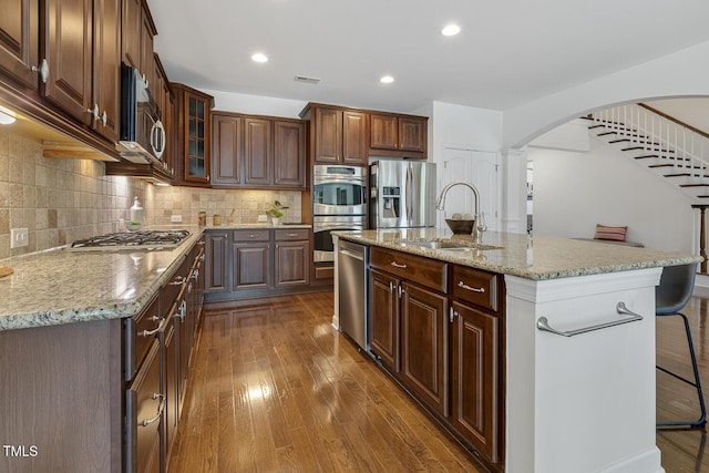 kitchen featuring arched walkways, a sink, decorative backsplash, dark wood-type flooring, and stainless steel appliances