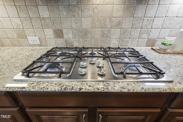 details featuring light stone countertops, tasteful backsplash, dark brown cabinets, and stainless steel gas cooktop