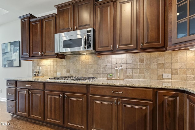 kitchen featuring dark brown cabinetry, backsplash, stainless steel appliances, and light stone countertops