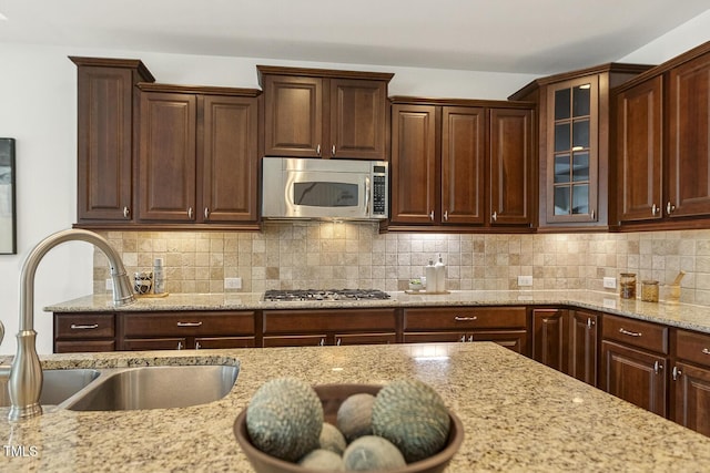 kitchen featuring a sink, stainless steel appliances, glass insert cabinets, and decorative backsplash