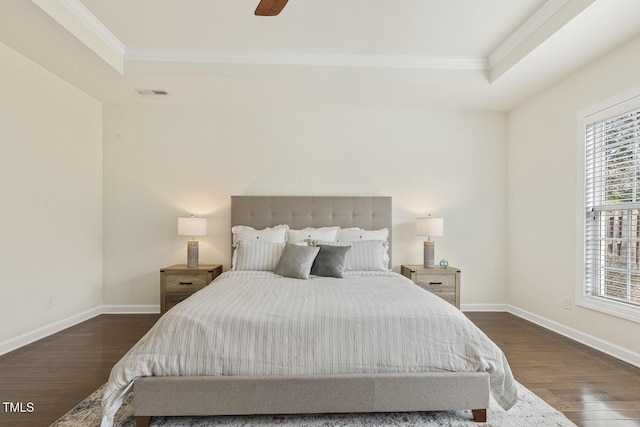 bedroom featuring a tray ceiling, baseboards, wood finished floors, and crown molding