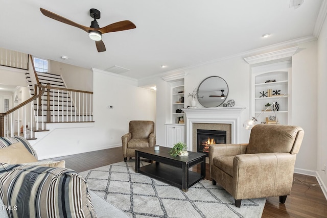 living area with built in shelves, a glass covered fireplace, wood finished floors, crown molding, and baseboards