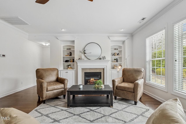 living area featuring visible vents, built in features, wood finished floors, and a glass covered fireplace