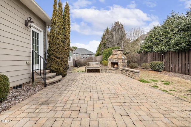 view of patio / terrace featuring entry steps, a fenced backyard, and an outdoor stone fireplace