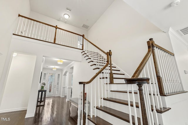 staircase featuring visible vents, a high ceiling, baseboards, and wood finished floors