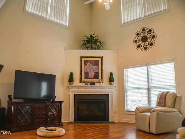 living area with ceiling fan, wood finished floors, a fireplace with flush hearth, and a towering ceiling