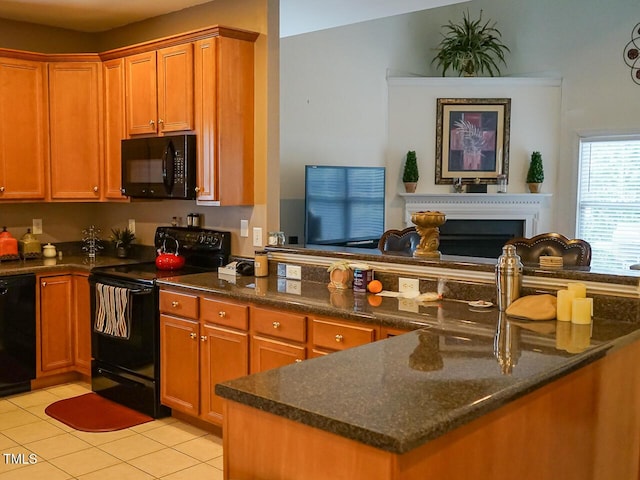 kitchen with light tile patterned floors, dark stone counters, brown cabinets, black appliances, and a fireplace