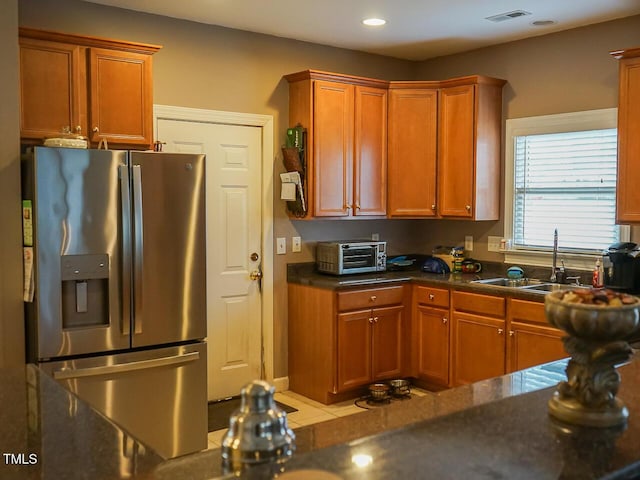 kitchen with a sink, visible vents, stainless steel fridge with ice dispenser, brown cabinets, and dark countertops