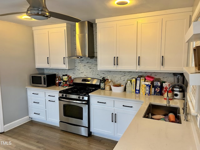 kitchen featuring wall chimney exhaust hood, appliances with stainless steel finishes, light countertops, and white cabinetry