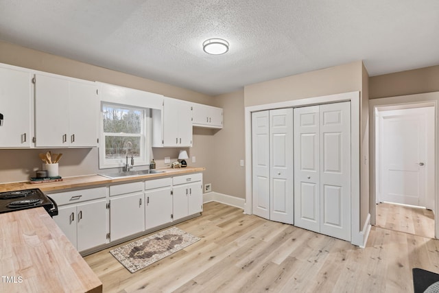 kitchen with butcher block countertops, a sink, light wood-style flooring, and white cabinetry