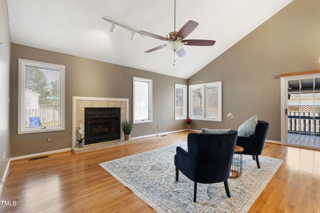 living room with visible vents, a tiled fireplace, light wood-style floors, a ceiling fan, and baseboards