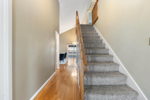 stairs featuring a chandelier, wood finished floors, lofted ceiling, and baseboards