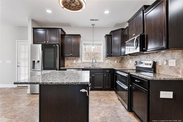 kitchen featuring stainless steel appliances, a kitchen island, a sink, visible vents, and light stone countertops