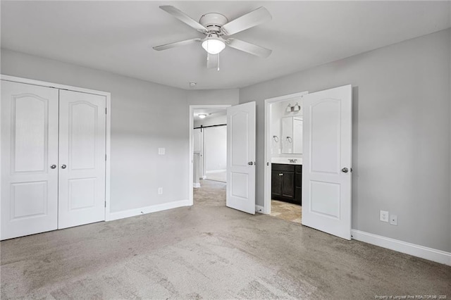 unfurnished bedroom featuring a barn door, baseboards, connected bathroom, carpet flooring, and a closet