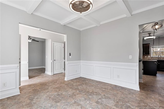 spare room with beamed ceiling, coffered ceiling, a wainscoted wall, a ceiling fan, and ornamental molding