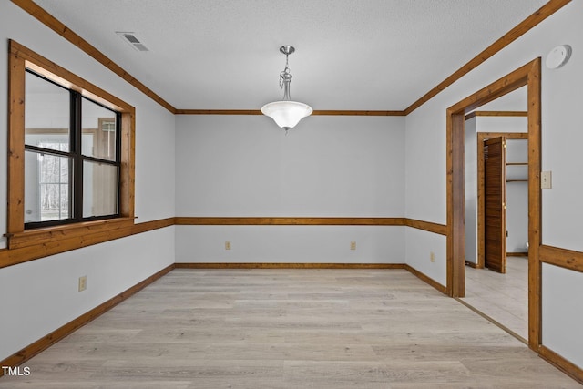 empty room featuring baseboards, light wood-style flooring, visible vents, and crown molding