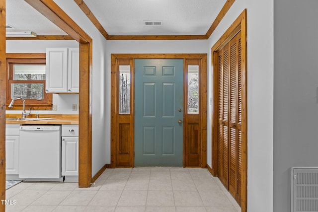 foyer with light tile patterned floors, baseboards, visible vents, and crown molding