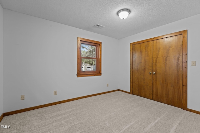 unfurnished bedroom with a textured ceiling, carpet floors, visible vents, baseboards, and a closet