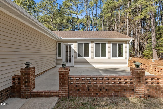 entrance to property featuring roof with shingles and a patio