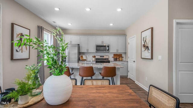 kitchen featuring decorative backsplash, a breakfast bar area, light stone countertops, a kitchen island with sink, and stainless steel appliances