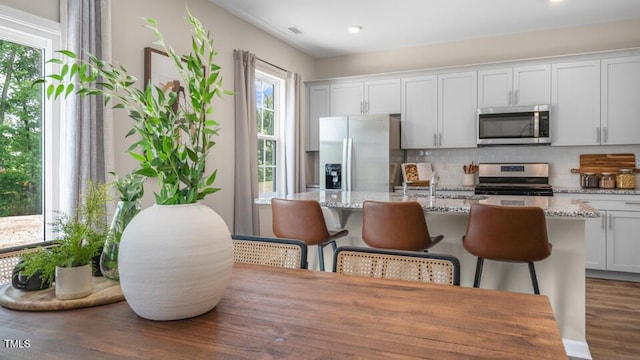 kitchen with stainless steel appliances, a center island with sink, a kitchen bar, and tasteful backsplash