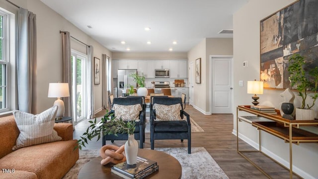 living area with recessed lighting, wood finished floors, visible vents, and baseboards