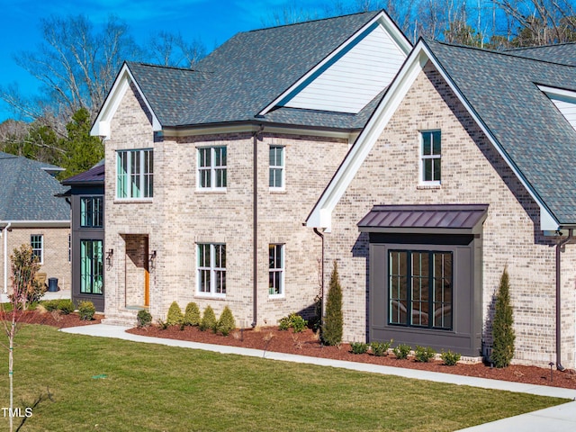 view of front of house featuring metal roof, a shingled roof, brick siding, a front lawn, and a standing seam roof