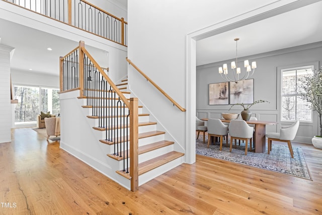 stairs with a notable chandelier, crown molding, a decorative wall, and wood finished floors