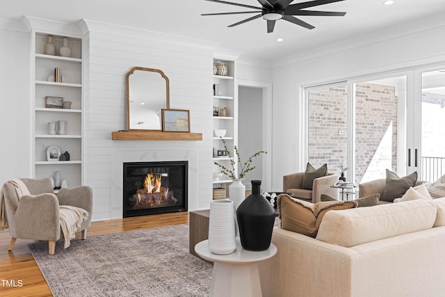 living room with built in shelves, crown molding, recessed lighting, a large fireplace, and wood finished floors