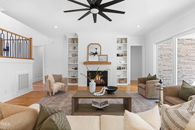 living area featuring a large fireplace, visible vents, crown molding, and wood finished floors