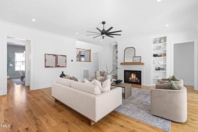 living room featuring built in shelves, light wood-type flooring, a fireplace, and baseboards