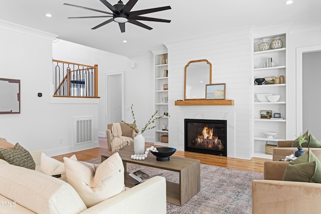 living area featuring recessed lighting, a fireplace, wood finished floors, visible vents, and crown molding